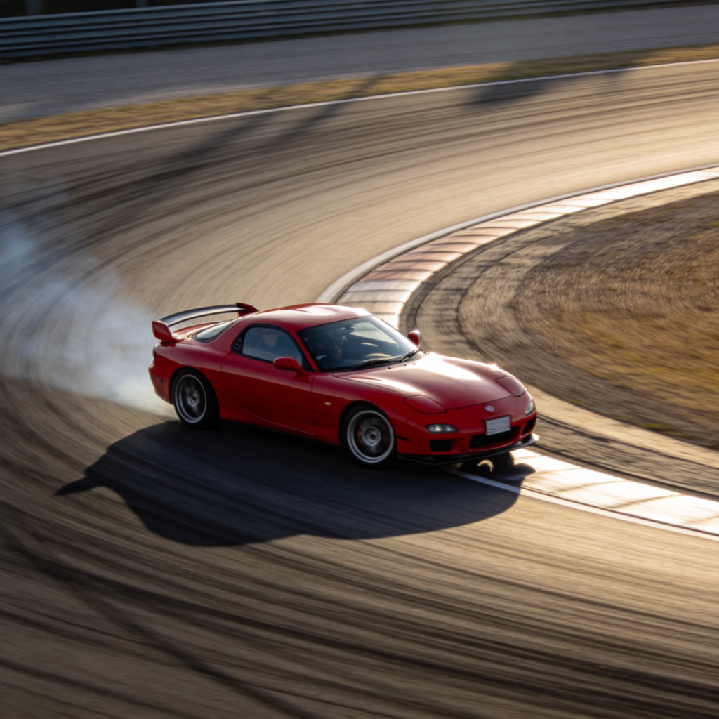 Dynamic action shot of a red sports car drifting around a sharp bend on a racetrack. The car is at an angle, with motion blur emphasizing speed and the curved trajectory. Focus on the car and the curve of the track.