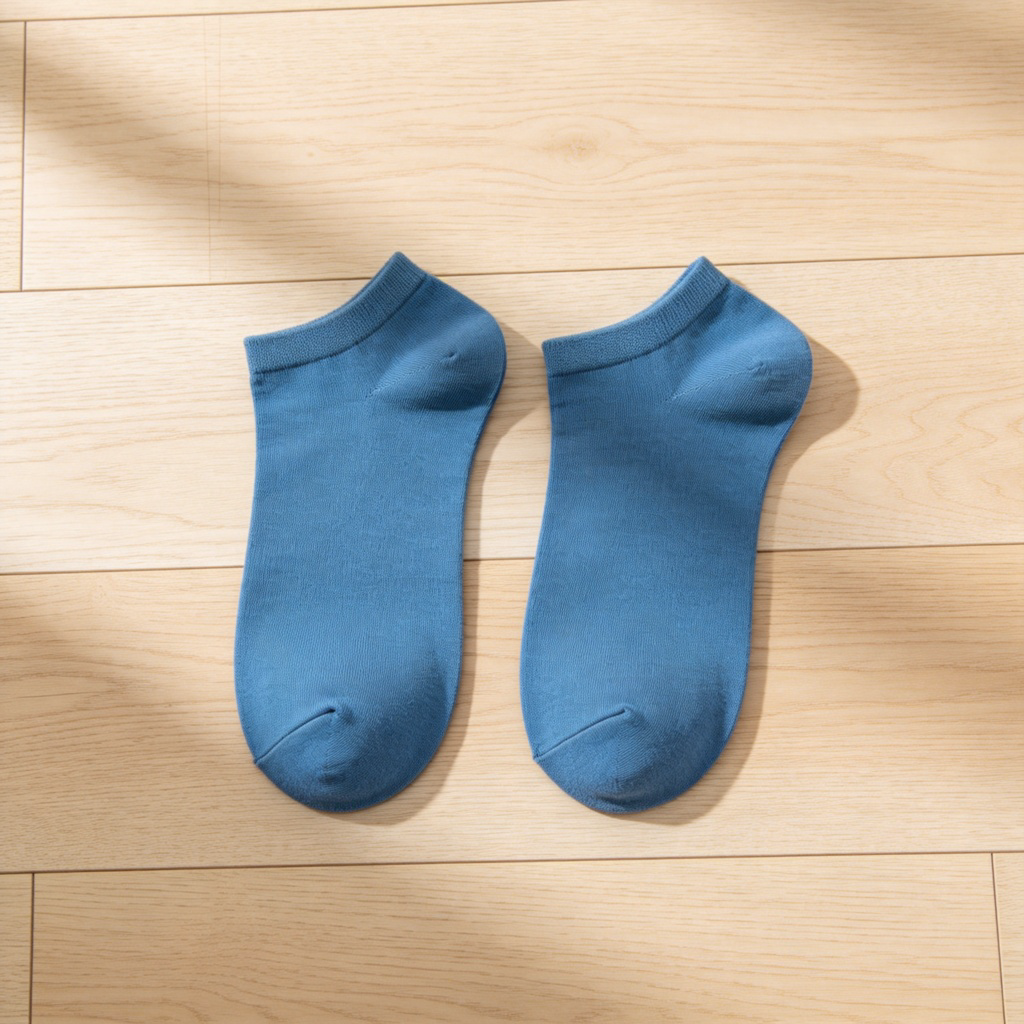 Two identical blue cotton socks placed neatly side by side on a light wooden floor. One sock is lying flat, the other is slightly turned to show its shape. Clean, minimalist composition with soft natural light, focusing on the sameness and partnership of the socks.