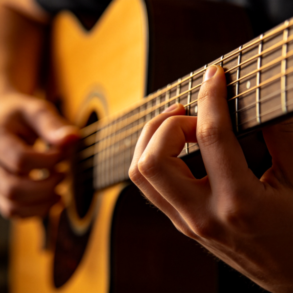 A close-up of hands playing an acoustic guitar. The focus is on the guitarist's expressive fingers on the strings, with the wooden body of the guitar slightly blurred in the background. The lighting is warm and intimate, suggesting deep emotion in the music. No text.